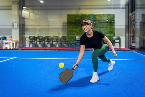 Woman playing pickleball on a vibrant blue indoor court, hitting the ball with her paddle during