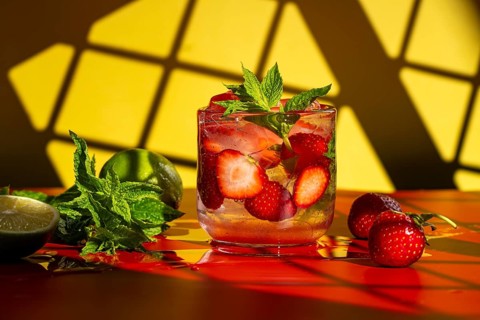 A vibrant strawberry mojito garnished with fresh mint and lime sits on a glossy red surface against