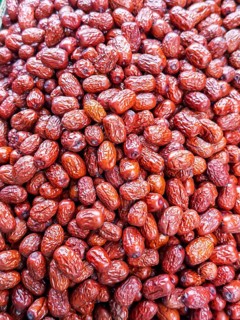 A vibrant close-up view of glossy, red jujube fruits, freshly harvested and displayed for sale at a