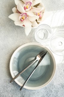 Stylish table setting features a textured ceramic plate, shiny cutlery, and delicate orchid flowers