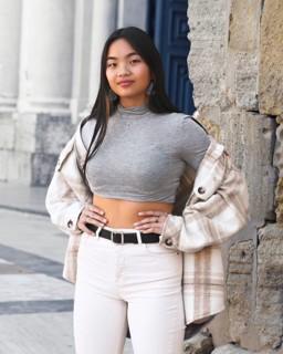 A young woman poses confidently in a chic urban setting, wearing a trendy plaid jacket over a gray