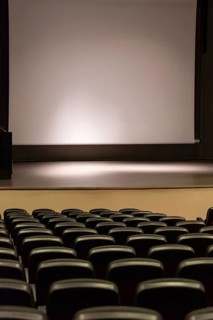 Rows of empty convention center seats facing a blank stage with a large screen, creating a quiet