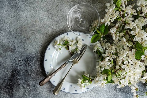 A table setting features vintage cutlery on a patterned plate, adorned with delicate white blossoms