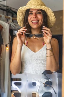 Happy tourist wearing straw hat trying on sunglasses in a souvenir shop in siargao island,