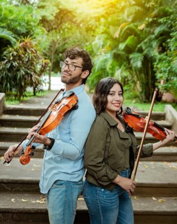 Portrait of two young violists back to back outdoors. Portrait of smiling male and female violinist