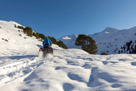 A man rides a snowmobile through a stunning winter mountain landscape, leaving a trail in the fresh