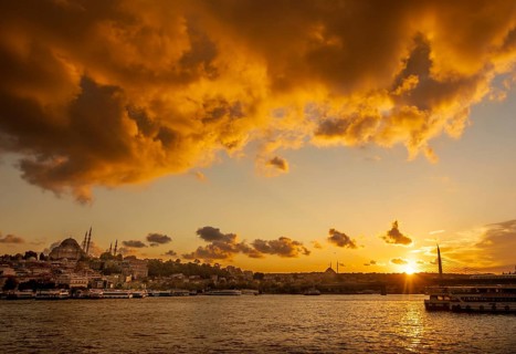 A vibrant sunset illuminates the sky above Istanbul, highlighting the silhouettes of mosques and a