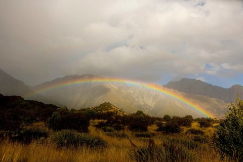 A breathtaking autumn scene at Mount Cook, New Zealand, featuring a vibrant rainbow arching over