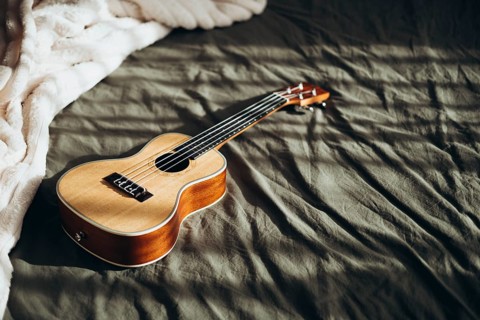 A wooden ukulele lies on a textured bedspread, illuminated by gentle natural light The warm tones