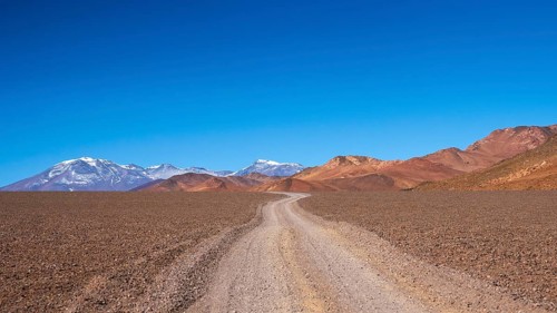 A captivating shot of a winding dirt road stretching through the stark, arid desert landscape of La