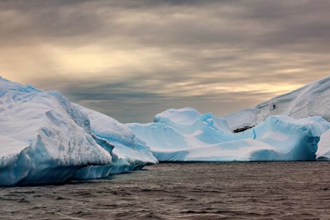 Huge, sharp icebergs stretch out under a cloudy sky as dusk falls, icebergs in the landscape of the