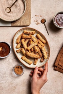Top view of cropped unrecognizable hand holding a ceramic plate filled with sugar-coated churros,