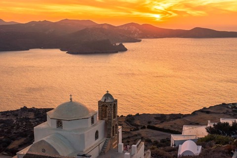 A serene sunset over the Greek coastline, featuring a classic white church with a dome in Plaka,