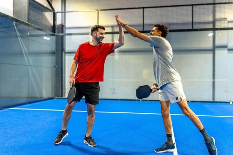 Male pickleball players celebrating victory and sportsmanship, high fiving on an indoor court after