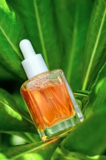 Dropper bottle of Vitamin C serum poised amidst vibrant green foliage, highlighting natural