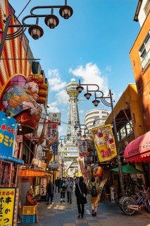Lots of colorful signs in a pedestrian zone with shops and restaurants, behind Tsutenkaku Tower,