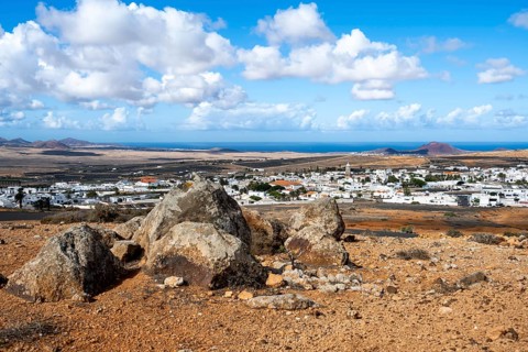 View of town, white houses of Teguise with church tower in dry volcanic landscape, view from