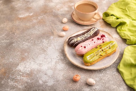 Glazed Eclairs on brown concrete background and green linen textile, cup of coffee, side view, copy