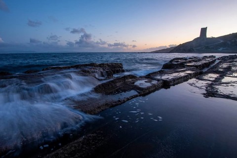 The serene sunset over the rocky coast of Tarifa, Cadiz, casts a soft glow on the water. Calm waves