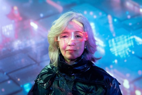 An elderly Asian woman dons futuristic eyewear, fully immersing herself in the vibrant, digital