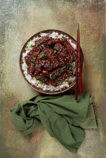 Crispy beef, with green onions and sesame seeds, on a rice pad, in a bowl with chopsticks, on a