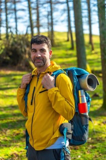 Male hiker carrying a backpack, enjoying a sunny day in the forest while trekking through the