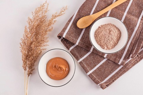 Top view of cosmetic clay powders in bowls beside an ornamental plant, presented with a wooden