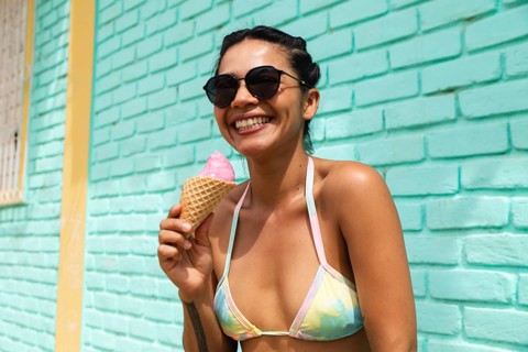 A joyful young Latin woman savors an ice cream cone under the sun in Mancora, Peru. Her bright