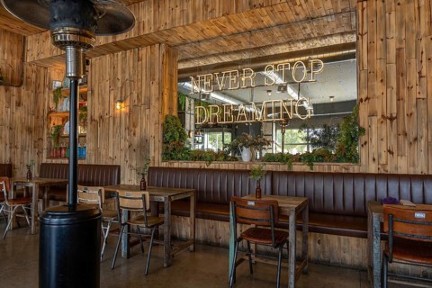 Warm, rustic cafe interior featuring wooden walls, vintage furniture, green plants, and a large