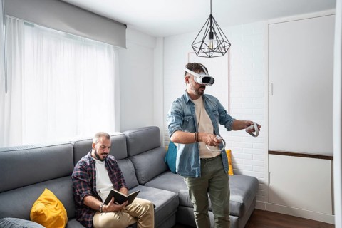 One man uses a VR headset, fully immersed in a virtual world, while his partner relaxes on the