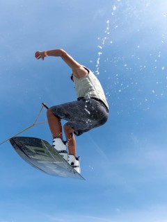 Young man jumping and flying with wakeboard, water sports and water skiing in the wakepark