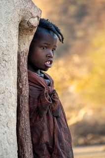 Himba girl leaning against a traditional mud hut, in the morning, traditional Himba village,