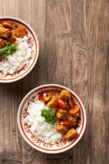 From above, two bowls of Hungarian pork goulash served with rice, garnished with a parsley leaf on
