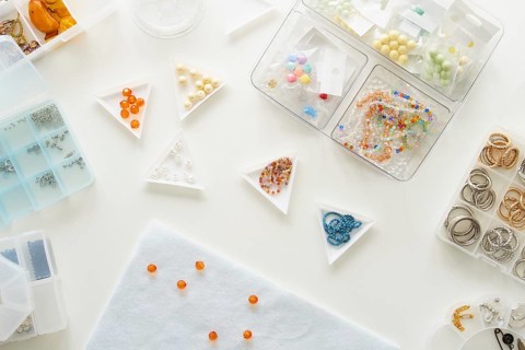Top view of a jewelry making studio setup featuring various beads and rings in organized containers