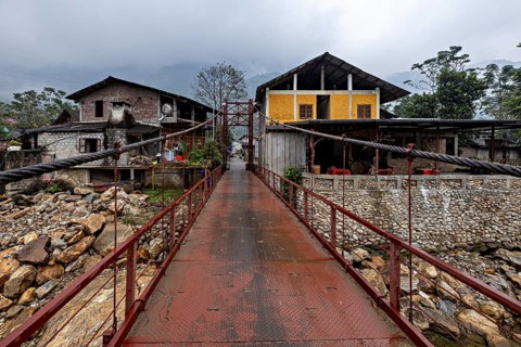 A metal bridge connects two older buildings, one of them yellow, under a grey cloudy sky, A bridge
