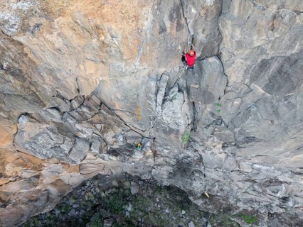 Two climbers in red gear expertly scales a rugged rock face using traditional climbing techniques.