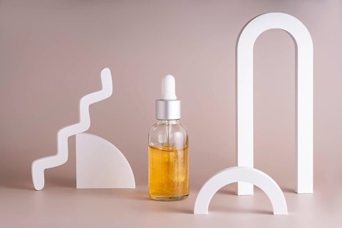 A modern cosmetic serum bottle with a silver dropper surrounded by minimalist geometric shapes on a