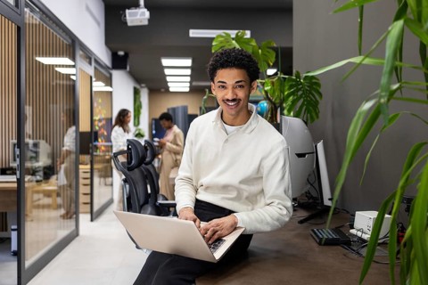 A modern office space features a smiling professional on a laptop, with colleagues interacting in