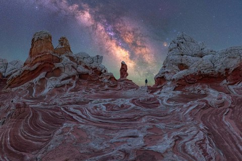 A lone man stands under the Milky Way, gazing at the stars over the unique geological formations of