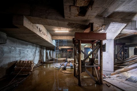A dimly lit basement under construction, with structural beams and tools scattered about. The work