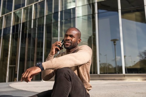 A cuban man sits outside a sleek, modern glass building, engaging in a conversation on their