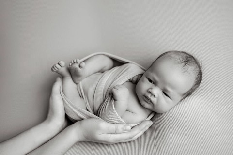 Cropped unrecognizable parent hands holding of a newborn baby securely . The baby appears calm and