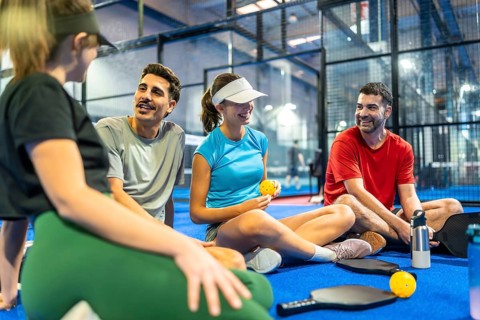 Group of diverse friends taking a break on an indoor pickleball court, smiling and having a social