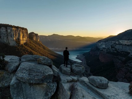 A lone figure stands on rocky cliffs, gazing over the Panta de Sau Reservoir in Catalonia, Spain,