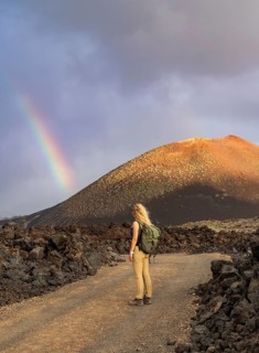 A woman with a backpack stands on a rocky path in Timanfaya National Park, Lanzarote. A vibrant