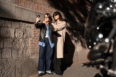 A multiethnic lesbian couple poses for a joyful outdoor selfie, exuding pride and love. The duo