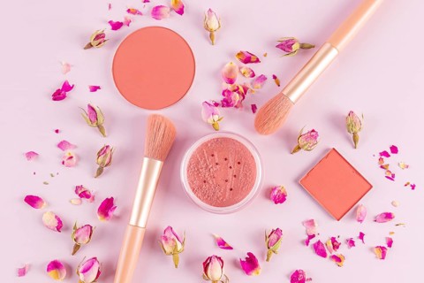 Aesthetic flat lay of pink makeup brushes and cosmetics surrounded by delicate rose petals on a