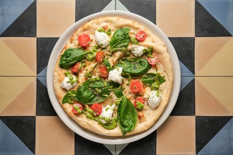 Top view of a delicious pizza with pesto, cherry tomatoes, basil and stracciatella cheese, served