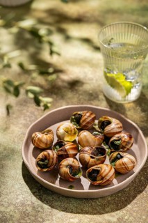 Gourmet baked escargots garnished with parsley and butter, served on a ceramic plate under natural