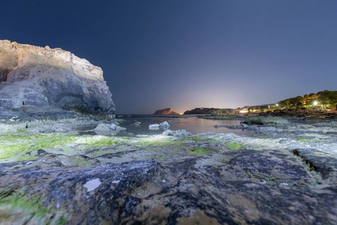 Tranquil Mediterranean shoreline on the Costa Blanca with rocky cliffs and calm sea under a starry